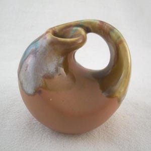 May include: A ceramic sculpture with a unique, organic shape. The piece features a loop and a rounded base, with a color palette of brown, gold, and hints of blue and purple. The sculpture has a glossy finish.