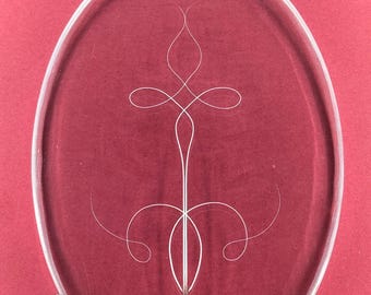 May include: A white pinstripe design is etched into a clear oval-shaped glass plate. The plate is mounted on a red background with four black screws.