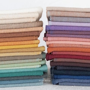 May include: Two stacks of folded fabric in a variety of colors. The left stack transitions from cream to shades of brown, yellow, green, and blue. The right stack features shades of pink, purple, orange, red, and blue. The word "FABLEISM" is visible at the bottom.