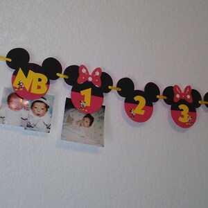 May include: A decorative banner featuring black and red mouse-shaped cutouts strung on a yellow ribbon. The cutouts display yellow numbers from NB to 5, with some featuring red bows and small character graphics. Two square photographs are attached.