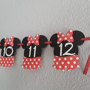 May include: A festive banner featuring black Minnie Mouse-shaped cutouts with red and white polka dot skirts and bows. Numbers 9, 10, 11, and 12 are displayed on the cutouts, perfect for a birthday celebration.