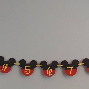 May include: A black and red Mickey Mouse themed banner with gold string. Each Mickey Mouse head has a number from 1 to 12 printed in yellow.