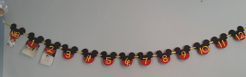May include: A black and red Mickey Mouse themed banner with gold string. Each Mickey Mouse head has a number from 1 to 12 printed in yellow.