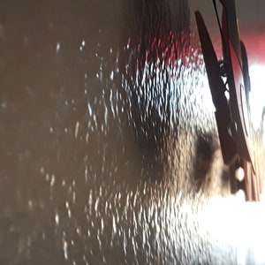 May include: A close-up of a textured wall with a white and red object hanging on it. The object is a clothespin with a metal spring.
