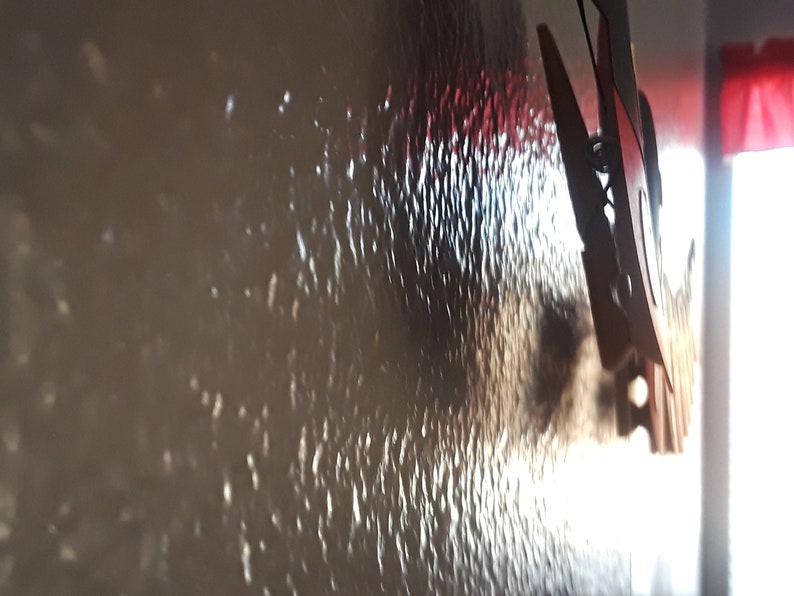 May include: A close-up of a textured wall with a white and red object hanging on it. The object is a clothespin with a metal spring.
