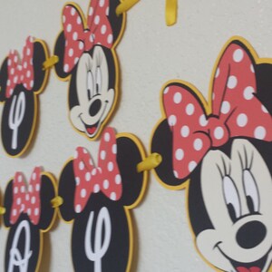 May include: A black and red Minnie Mouse themed banner with the word "Happy" in white letters. The banner is made of cardstock and has yellow string connecting the pieces.