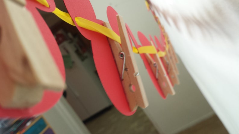 Pu&ograve; includere: Una ghirlanda decorativa con ritagli di carta rossi circolari sospesi a un nastro giallo brillante. Ogni cerchio di carta rossa &egrave; fissato al nastro giallo utilizzando una piccola molletta in legno naturale con una molla in metallo.