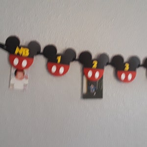 May include: A black and red Mickey Mouse themed banner with numbers 1 through 4 and the letters "MB". The banner is strung with black string and has white circles on each Mickey Mouse head.