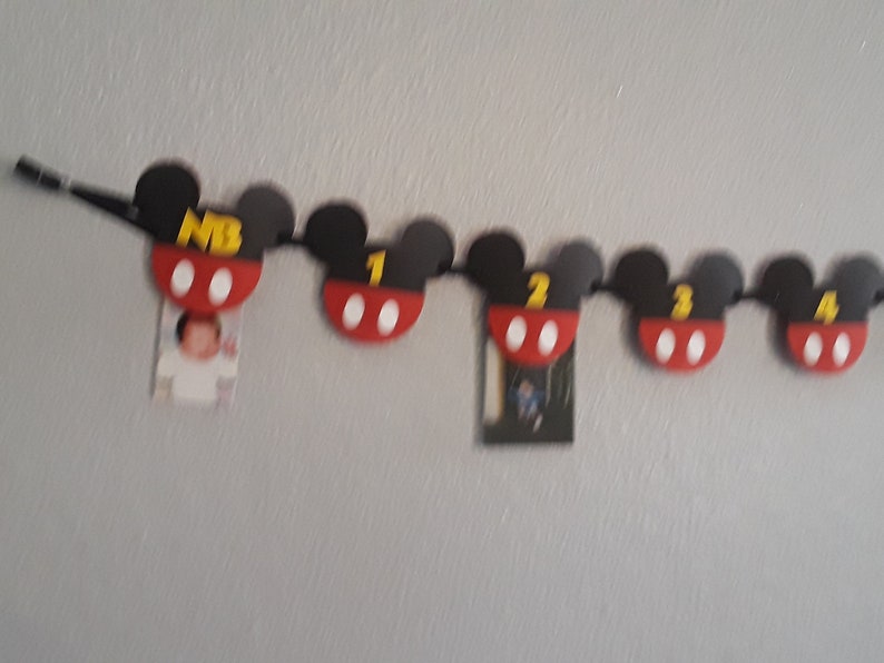 May include: A black and red Mickey Mouse themed banner with numbers 1 through 4 and the letters "MB". The banner is strung with black string and has white circles on each Mickey Mouse head.