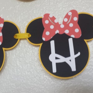 May include: A black and yellow Minnie Mouse themed banner with the letter "H" in white. The banner is made of felt and has red and white polka dot bows.