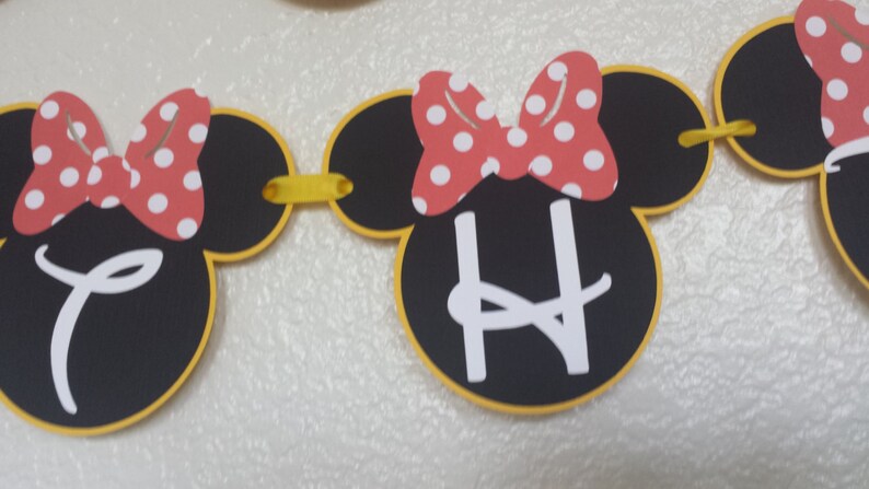 May include: A black and yellow Minnie Mouse themed banner with the letter "H" in white. The banner is made of felt and has red and white polka dot bows.