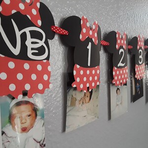 May include: A Minnie Mouse-themed photo banner with black cutouts shaped like Minnie's head, red polka-dot skirts, and white numbers. The banner displays photos and the letters "NB" and numbers 1 through 6.