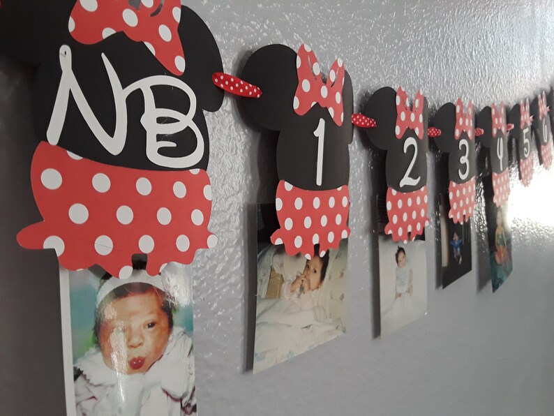 May include: A Minnie Mouse-themed photo banner with black cutouts shaped like Minnie's head, red polka-dot skirts, and white numbers. The banner displays photos and the letters "NB" and numbers 1 through 6.