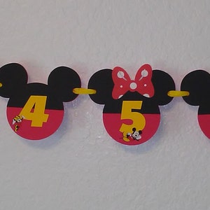 May include: A decorative banner featuring black Mickey Mouse-shaped silhouettes with red bottoms and yellow numbers 3, 4, 5, and 6. Some silhouettes feature a red bow with white polka dots and small illustrations of Minnie Mouse at the base of the numbers.