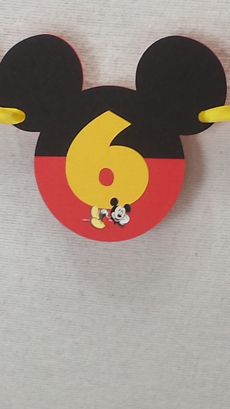 Pu&ograve; includere: Una sagoma decorativa a forma di testa di Topolino, con la parte superiore nera e quella inferiore rossa. Un grande numero sei giallo &egrave; centrato sulla parte anteriore, con una piccola illustrazione di Topolino alla base del numero.
