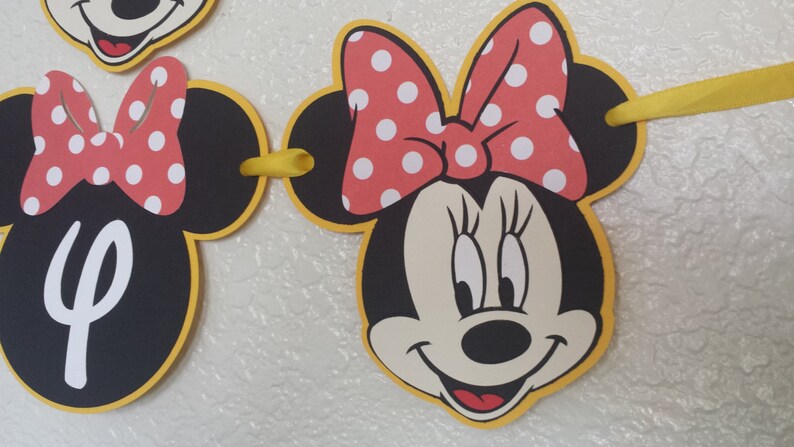 May include: A black and yellow Minnie Mouse banner with red polka dot bows. The banner has a yellow ribbon connecting the pieces.