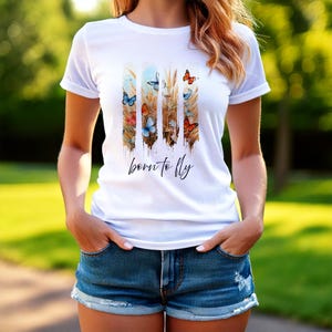May include: White t-shirt with a graphic of wheat stalks and butterflies in shades of blue, orange, and yellow. The text "born to fly" is printed below the graphic.