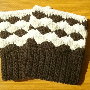 Puede incluir: Calentadores de piernas de crochet marrón y blanco con un patrón texturizado. Los calentadores de piernas están hechos con un hilo grueso y tienen un puño acanalado.
