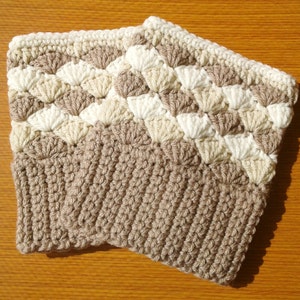 Puede incluir: Un par de polainas de ganchillo en beige, crema y blanco. Las polainas están hechas con un patrón de punto texturizado.