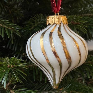 Op de afbeelding: Witte kerstbal met gouden strepen. De bal is traanvormig en heeft een gouden top.