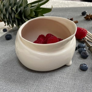 Może przedstawiać: Biała ceramiczna miska o unikalnym, falistym wzorze. Miska jest wypełniona świeżymi czerwonymi malinami.