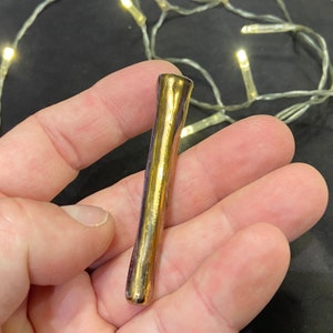 May include: A gold-colored ceramic pipe with a smooth, shiny finish. The pipe is about 4 inches long and has a rounded end.
