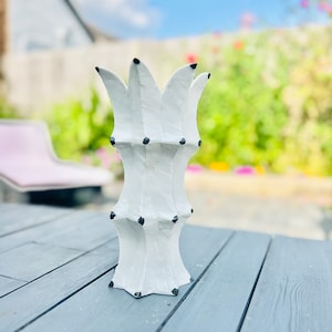 Op de afbeelding: Witte keramische vaas met een geometrisch ontwerp en zwarte accenten. De vaas heeft een hoge, slanke vorm en een brede opening aan de bovenkant.