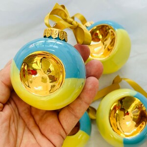 May include: Four yellow and blue Christmas ornaments with gold accents. Each ornament has a circular gold design in the center.