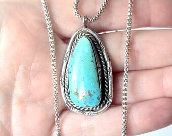 May include: A teardrop-shaped turquoise pendant set in a silver frame with twisted wire and stamped detailing. The pendant hangs from a silver box chain necklace. The turquoise stone is light blue with dark brown matrix inclusions throughout.