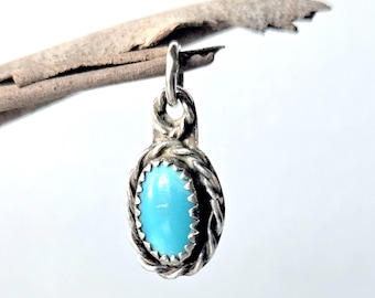 May include: A small oval pendant featuring a bright blue turquoise stone set in a serrated silver bezel. The stone is surrounded by a twisted rope-style silver border and includes a small silver jump ring at the top for attachment to a chain.