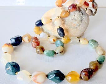 May include: A necklace composed of polished, irregularly shaped stones in various colors including shades of blue, green, yellow, orange, and white. The smooth, rounded beads are strung together with small metallic spacers between each individual stone.