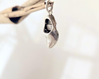 May include: A small, polished silver charm shaped like a traditional Dutch wooden clog. The charm features a smooth, metallic finish and includes a small circular jump ring at the top for attachment to a bracelet or necklace chain.