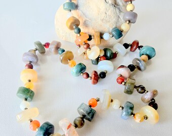 May include: A necklace and bracelet set featuring smooth, multi-colored stone beads in shades of green, orange, yellow, white, and brown. The beads are interspersed with small metallic spacers, creating a varied, polished appearance throughout.