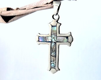 May include: A silver-toned metal cross pendant featuring inlaid iridescent abalone shell segments. The cross has a smooth, polished border and a central vertical and horizontal inlay of multi-colored, shimmering shell pieces with blue and green hues.
