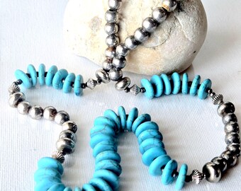 May include: A necklace featuring a strand of round, polished silver-toned beads alternating with flat, circular turquoise-colored stone discs. The design includes small, ribbed silver-toned spacers between the beads and stones, finished with silver-toned cones.
