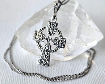 May include: A silver-toned Celtic cross pendant necklace featuring intricate marcasite stone inlay. The cross design includes a central circle and is suspended from a delicate silver-toned chain, showcasing a metallic finish and detailed craftsmanship.