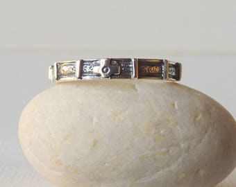 May include: A silver band ring featuring a repeating pattern of small, raised cross motifs separated by vertical bars. The metal has a polished finish on the raised sections and a darkened, oxidized texture within the recessed areas of the band.