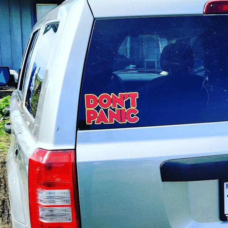 May include: A silver car with a red and yellow "Don't Panic" sticker on the back window.
