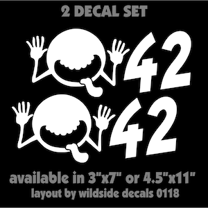 May include: A set of two white vinyl decals featuring the number 42 and a cartoon character with a wide grin and tongue sticking out. The decals are available in two sizes: 3 inches by 7 inches or 4.5 inches by 11 inches. The text "2 DECAL SET" is at the top of the image. The text "available in 3"x7" or 4.5"x11" layout by wildside decals 0118" is at the bottom of the image.