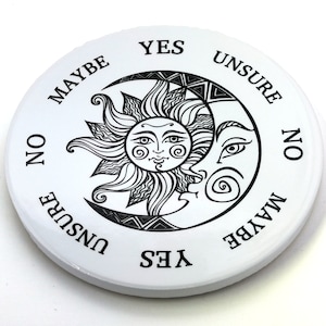 May include: A white circular divination board with black text and a black and white illustration of a sun and moon. The text reads "YES", "MAYBE", "NO", "UNSURE", and "YES" again.