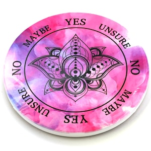 May include: A pink and purple circular divination board with a black lotus mandala design. The board has the words "YES", "MAYBE", "NO", "UNSURE" written around the edge.