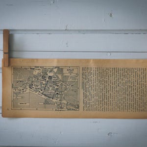 Puede incluir: Se muestra un mapa antiguo de Split, Croacia, con texto adjunto. El mapa, impreso en tinta negra, está sujeto a un tendedero con pinzas de madera. El papel tiene un aspecto amarillento y envejecido, lo que sugiere que es antiguo.