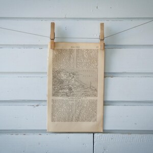 Può includere: Un'illustrazione in bianco e nero di una città o di un paese, stampata su un foglio di carta e appesa a un muro bianco con due mollette di legno.