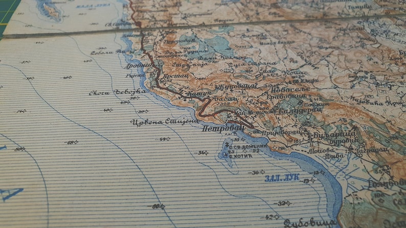 May include: A detailed vintage map with a coastal region, featuring shades of brown, blue, and beige. The map includes geographical features, place names, and contour lines, suggesting a historical or antique cartographic piece.