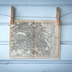 Peut inclure: Une carte en noir et blanc de Liège, en Belgique, accrochée à un mur bleu clair avec deux pinces à linge en bois.