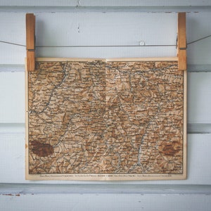 Könnte beinhalten: Eine Vintage-Karte einer Region, die an einer weißen Holzwand mit zwei Holz-Wäscheklammern hängt.