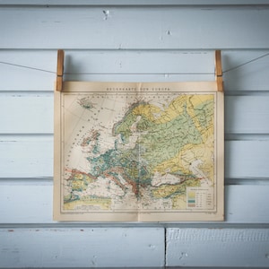 Puede incluir: Un mapa vintage de Europa colgado en una pared de madera azul claro con dos pinzas de madera. El mapa está titulado "REGIONSKARTE VON EUROPA".