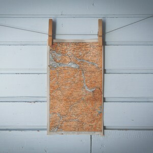 May include: A vintage map of a region is hanging on a white wooden wall with two wooden clothes pegs.