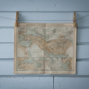 Puede incluir: Un mapa antiguo del Imperio de Alejandro Magno, colgado en una pared azul claro con pinzas de madera.