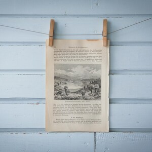 Puede incluir: Una ilustración vintage en blanco y negro de un paisaje con árboles y un río. La ilustración está impresa en un trozo de papel y está colgada en una pared azul claro con dos pinzas de madera.